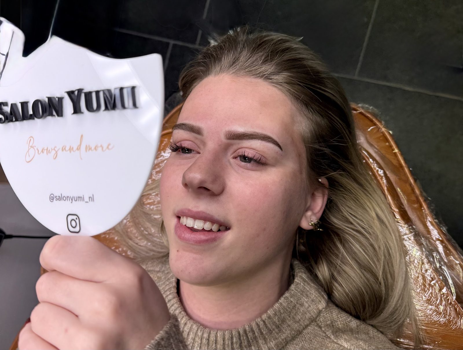 Klant bekijkt haar nieuwe wenkbrauwen in de Salon Yumi spiegel
